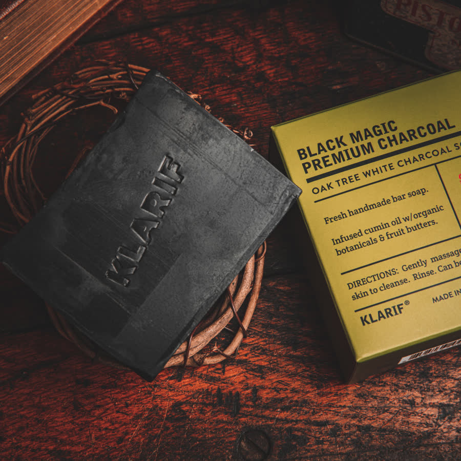 Klarif Black Magic charcoal soap bar beside its kraft box on dark wood